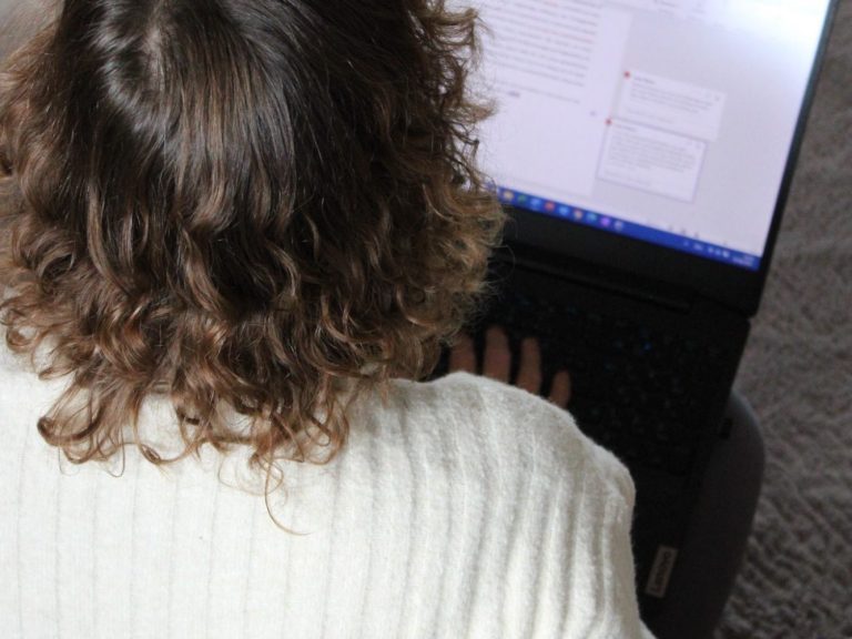 Paket Feinschliff Person mit lockigem Haar tippt auf einem Laptop.