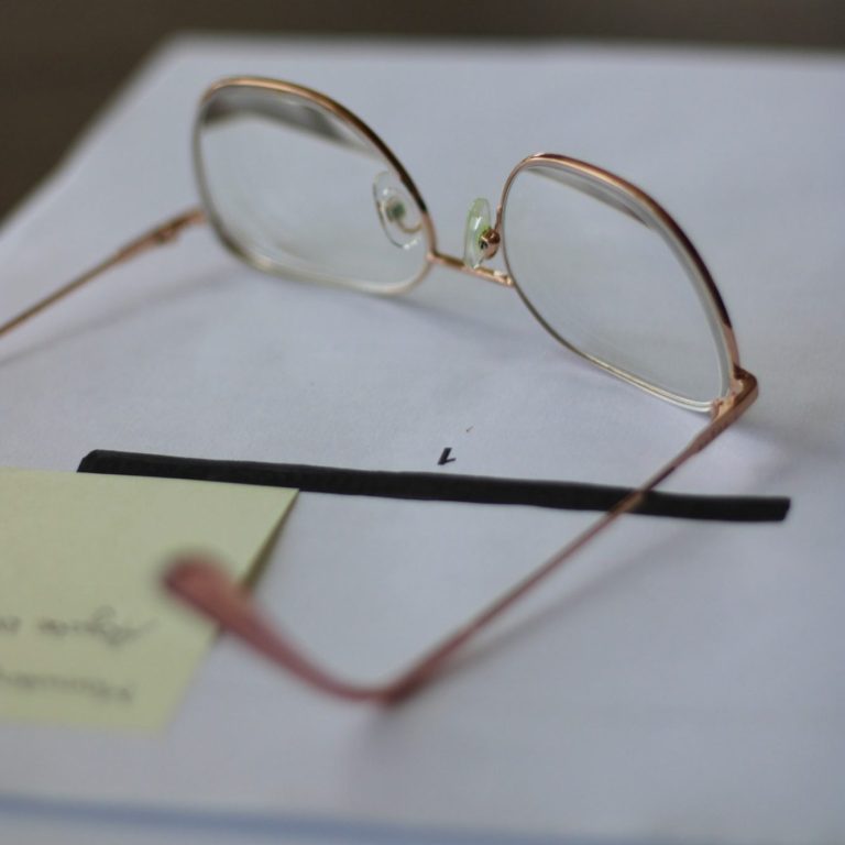 Paket Kapitelherz Roséfarbene Brille liegt auf einem Stapel Papier mit einem Post-it-Zettel.