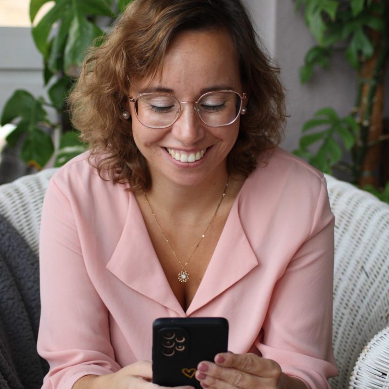 Welches Paket passt zu mir? Lächelnde Frau mit Brille, die auf ihrem Smartphone tippt, umgeben von Pflanzen.